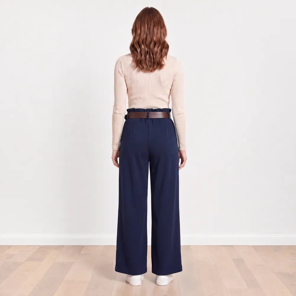 Back view of navy Ellana wide-leg paperbag-waist trousers with brown leather belt, cream ribbed knit top and white trainers