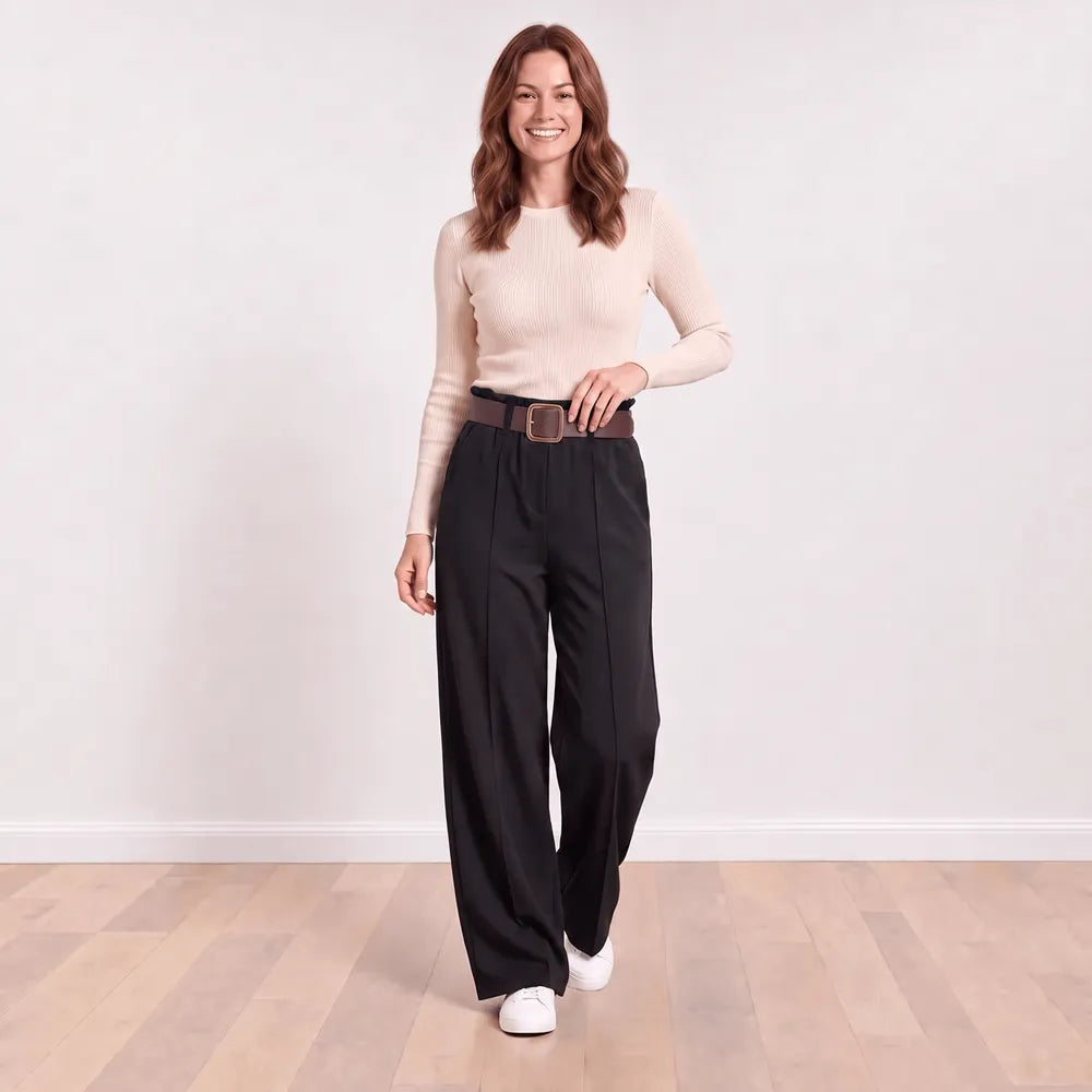 Ellana wide-leg pleated trousers in black with hand resting on the brown belt buckle, showing the waistband frill