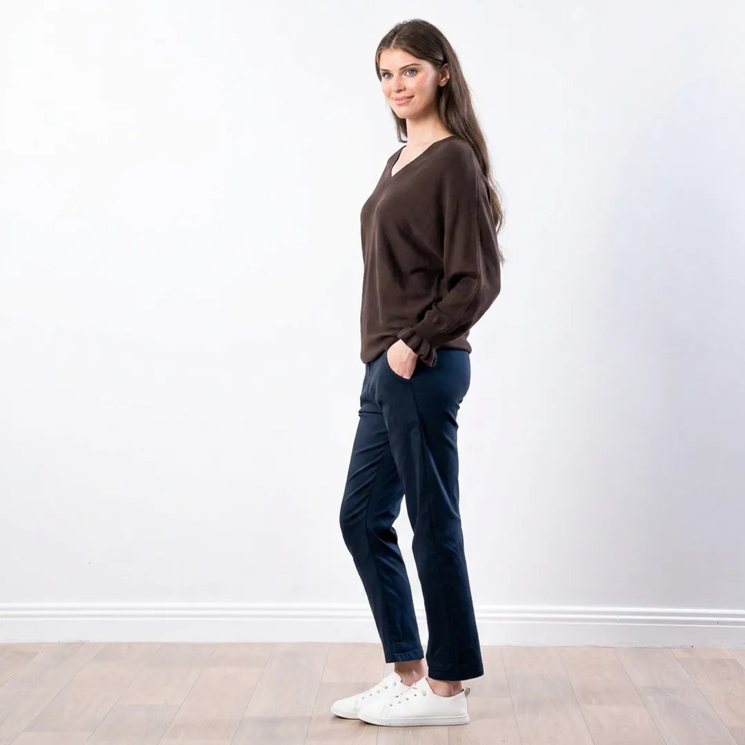 Side profile of chocolate brown Lexie batwing V-neck knit top with navy trousers and white trainers
