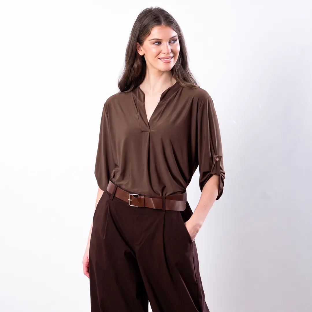 Sharlene Top in brown — waist-up three-quarter view with hand in pocket, showing buttoned roll-tab sleeve detail and brown leather belt