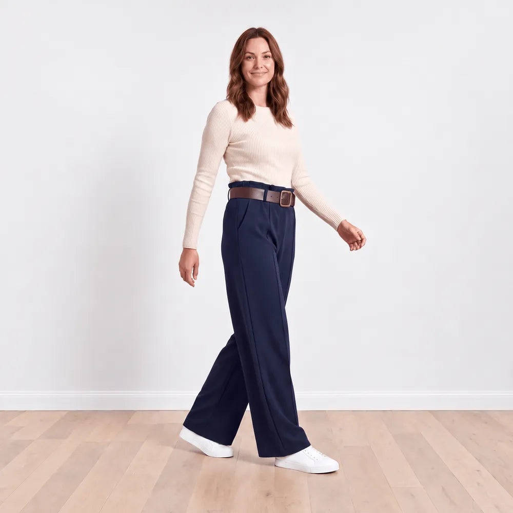 Model walking in navy Ellana wide-leg trousers with brown belt and cream knit top, showing the leg drape in motion