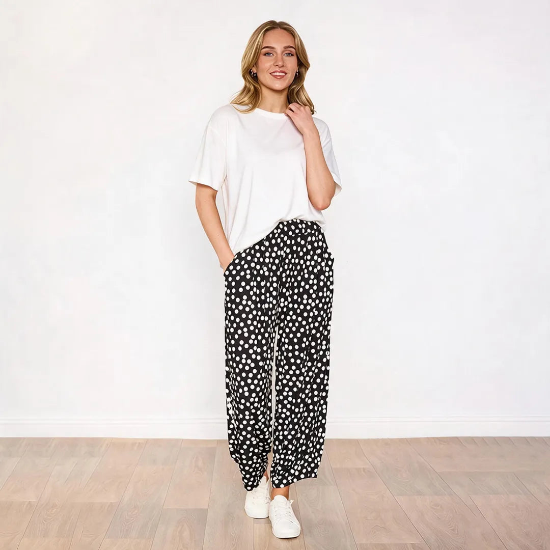 Model in white tee and Fraya black polka dot trousers, hand to shoulder styling pose