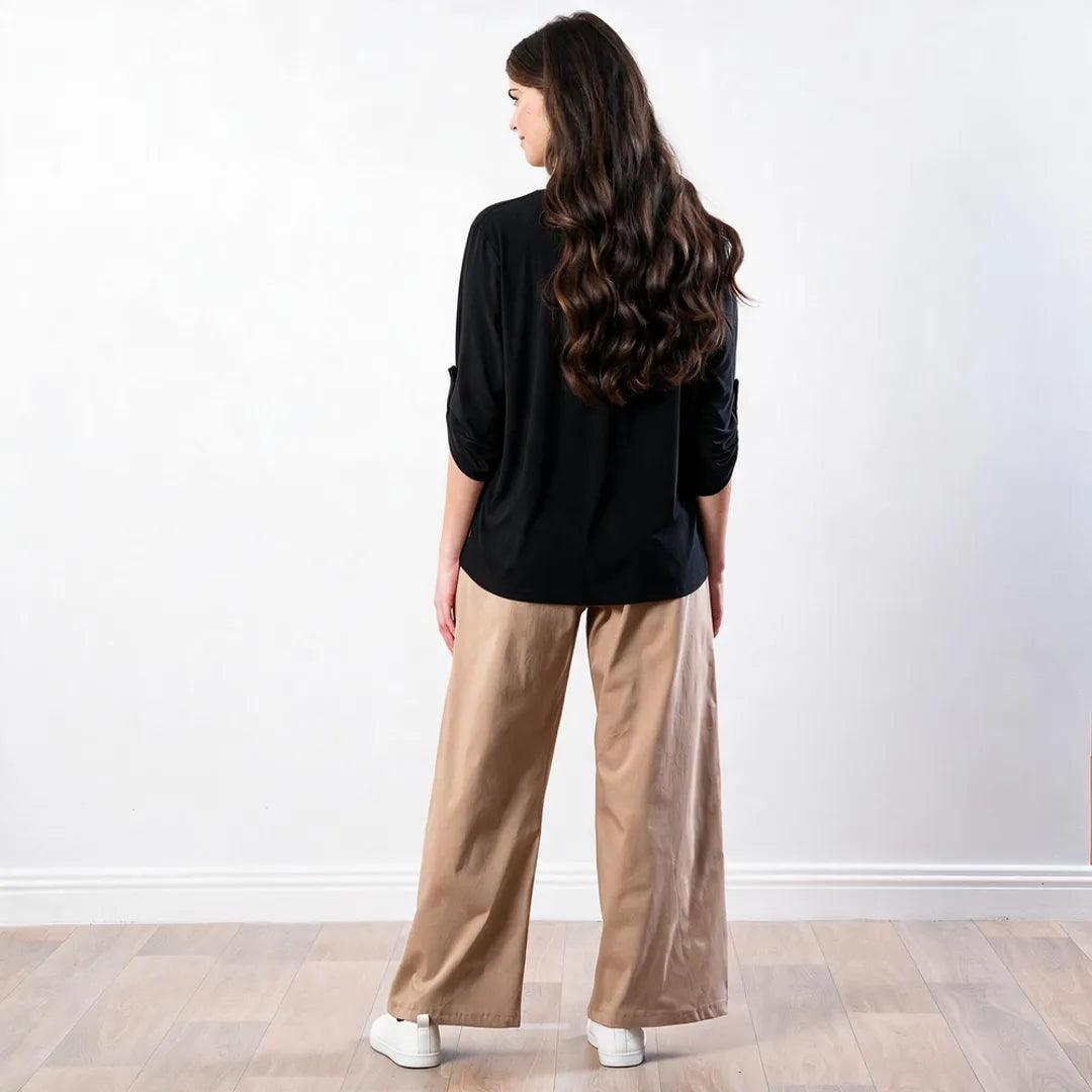 Sharlene Top in black — back view showing curved hem and shoulder line, styled with tan wide-leg trousers