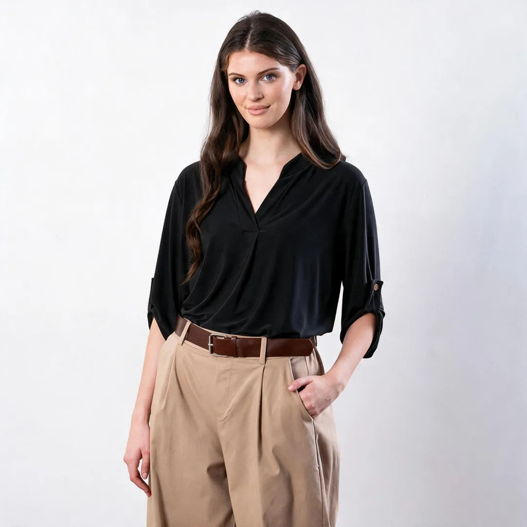 Sharlene Top in black — relaxed front view with hand in pocket, showing tab-roll sleeve detail with tan button