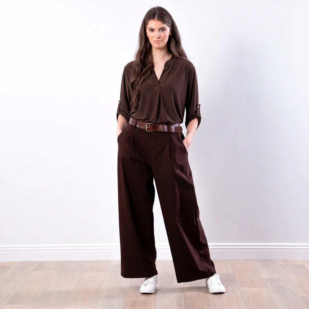 Sharlene Top in brown — relaxed jersey blouse with roll-tab sleeves and centre-front pleat, worn with brown wide-leg pleated trousers, full-length front view