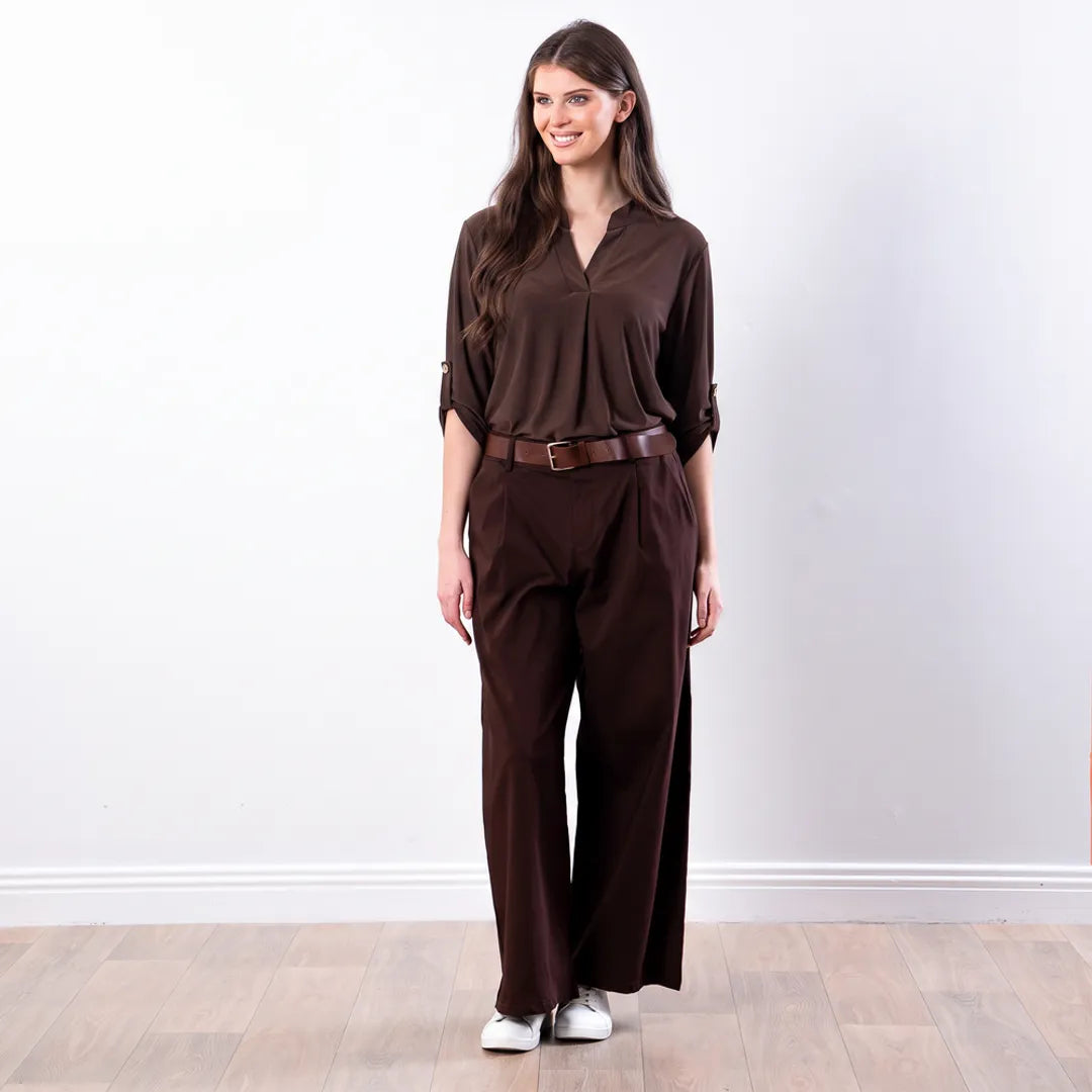 Sharlene Top in brown — relaxed jersey blouse with notch V neckline, arms relaxed, styled with brown wide-leg trousers and white trainers, full-length front view