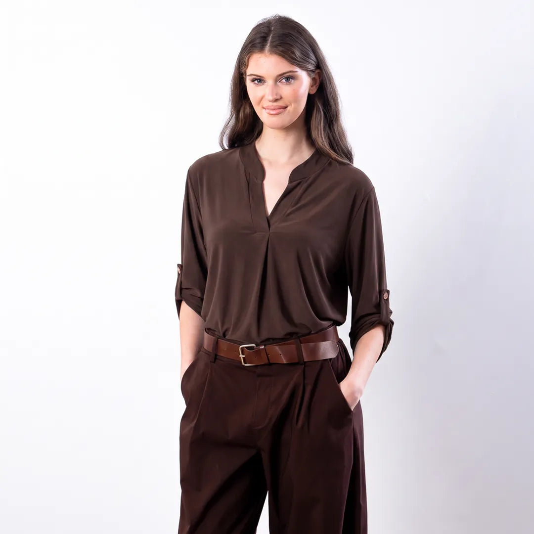 Sharlene Top in brown — close waist-up view showing notch V mandarin collar, centre-front pleat and buttoned roll-tab sleeve, worn with brown leather belt